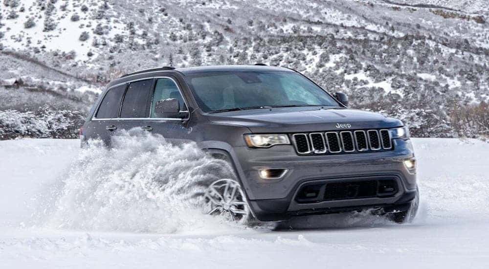 A gray 2020 Jeep Grand Cherokee North Edition is kicking up snow in the mountains.