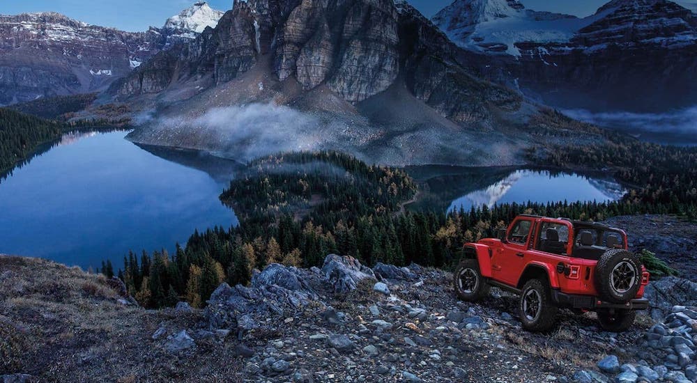 A red 2020 Jeep Wrangler is perched atop a mountain overlooking a majestic pond.