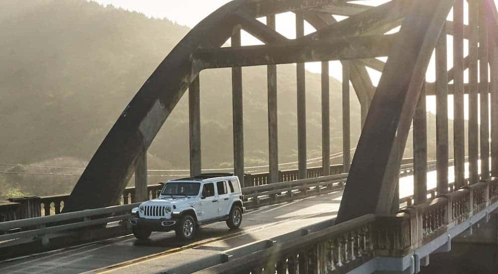 A white 2020 Jeep Wrangler Unlimited is driving over a misty bridge.