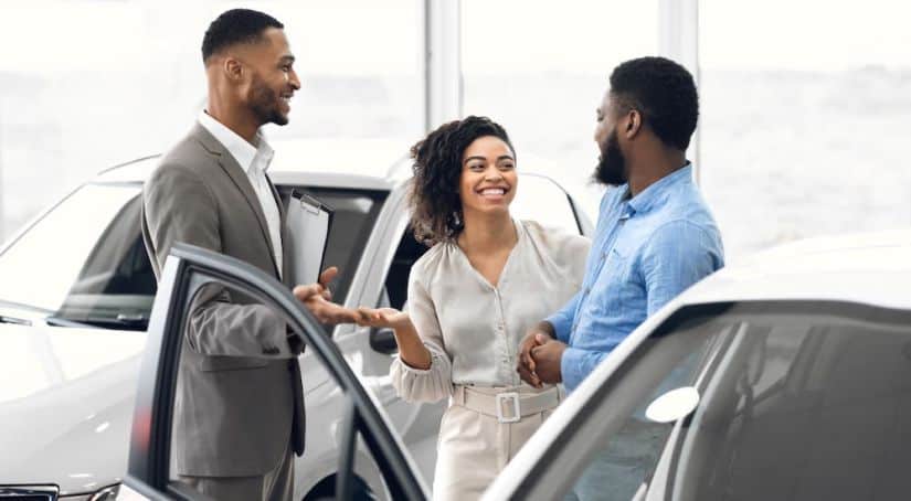 A salesman is showing a smiling couple a car in an Ohio car dealer showroom.