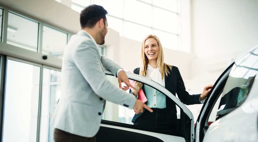 A woman is showing a man a car in a dealership.