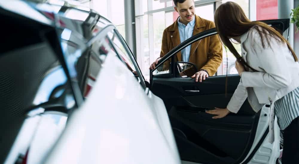 A woman is looking at the interior of a white used car next to a salesman.