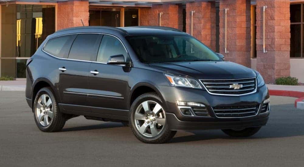 A gray 2014 Chevy Traverse is parked in front of a brick building.