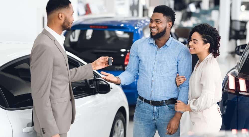 A salesman is talking to a couple at a used car dealership.