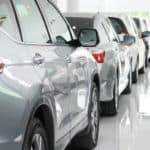 A row of silver and white used cars for sale are in a bright dealership.