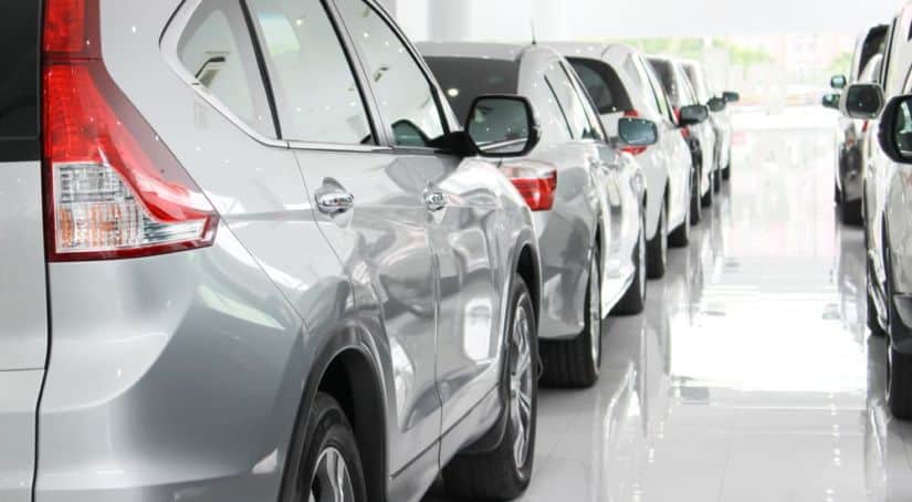 A row of silver and white used cars for sale are in a bright dealership.