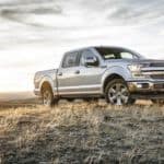 A silver 2018 Ford F-150 is parked off-road with distant mountains behind it.
