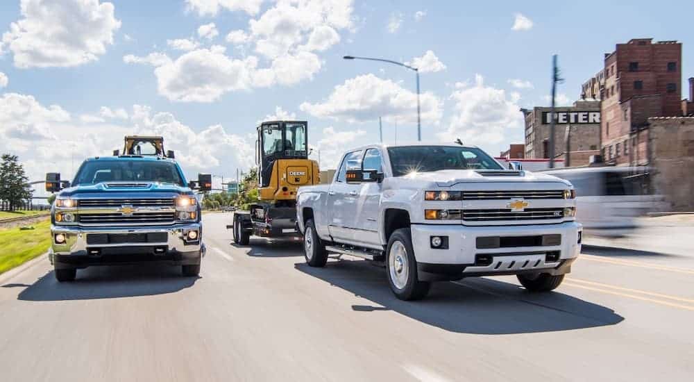 A black and a white 2018 Chevy Silverado 2500HD are towing equipment side by side.