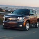 A brown 2020 Chevy Tahoe is driving around a corner with a city in the distance after winning the 2020 Chevy Tahoe vs 2020 Nissan Armada comparison.