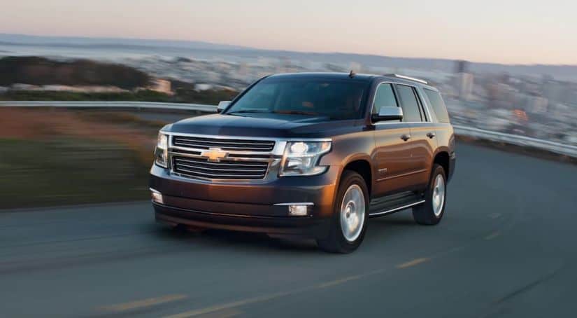 A brown 2020 Chevy Tahoe is driving around a corner with a city in the distance after winning the 2020 Chevy Tahoe vs 2020 Nissan Armada comparison.