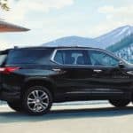 A black 2020 Chevy Traverse, which wins when comparing the 2020 Chevy Traverse vs 2020 Honda Pilot, is parked outside a mountain home.
