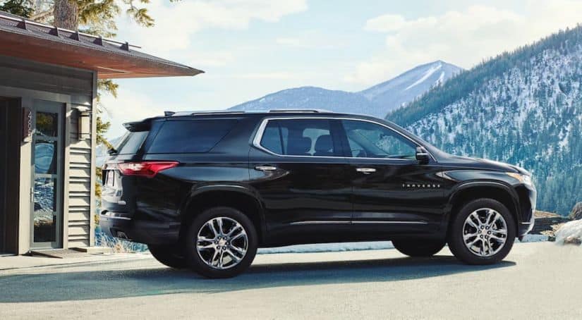 A black 2020 Chevy Traverse, which wins when comparing the 2020 Chevy Traverse vs 2020 Honda Pilot, is parked outside a mountain home.