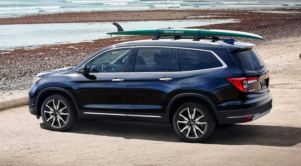 A blue 2020 Honda Pilot is parked at a beach with a surf board on the roof.