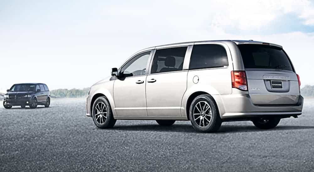 A silver and a black 2020 Dodge Grand Caravan are parked in an open area with a light sky.