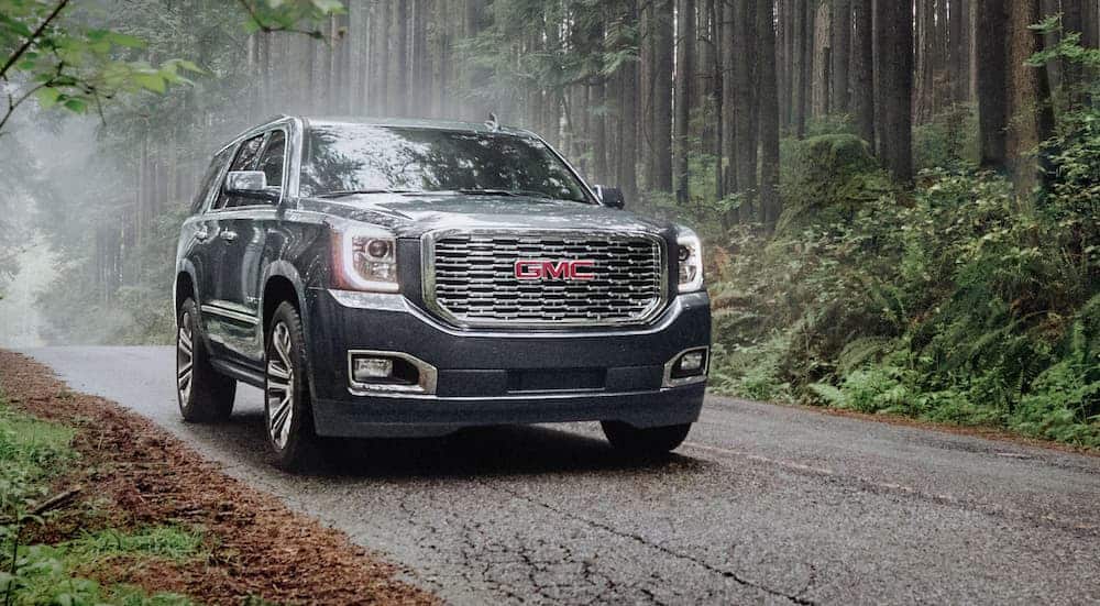 A grey 2020 GMC Yukon is on a tree-lined road in the rain.