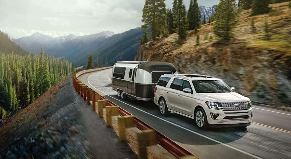 A white 2020 Ford Expedition is towing a camper on a winding mountain road after winning the 2020 Ford Expedition vs 2020 Nissan Armada comparison.
