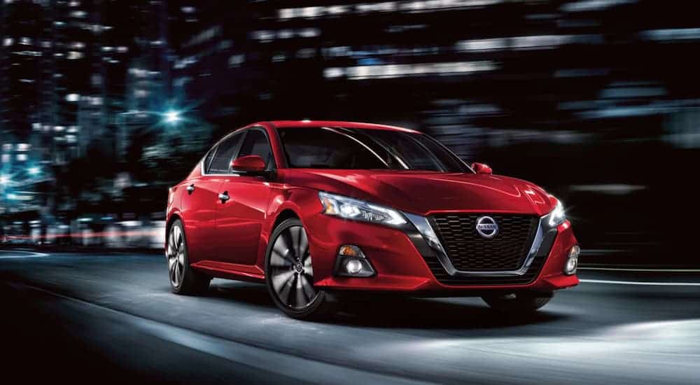A red 2020 Nissan Altima is driving on a city street at night.