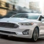 A white 2020 Ford Fusion is driving on a blurred city street after winning the 2020 Ford Fusion vs 2020 Nissan Altima comparison.