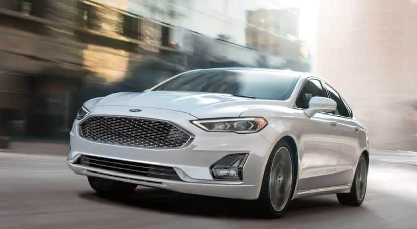 A white 2020 Ford Fusion is driving on a blurred city street after winning the 2020 Ford Fusion vs 2020 Nissan Altima comparison.