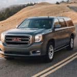 A grey 2020 GMC Yukon is driving on a winding road along a hill after winning the 2020 GMC Yukon vs 2020 Chevy Tahoe comparison.