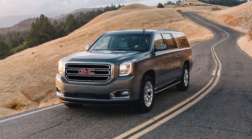 A grey 2020 GMC Yukon is driving on a winding road along a hill after winning the 2020 GMC Yukon vs 2020 Chevy Tahoe comparison.
