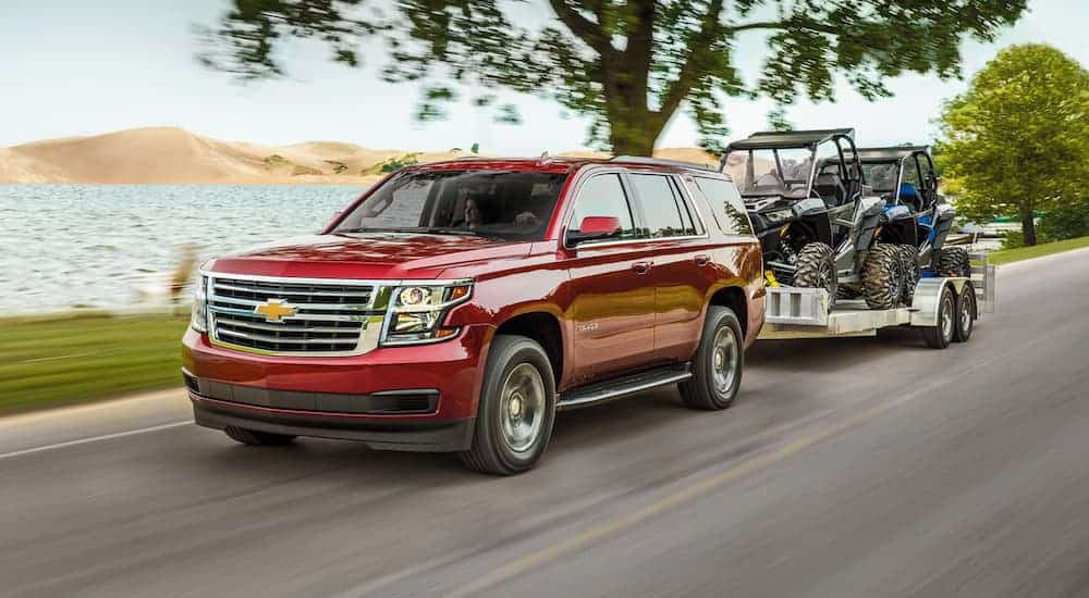 A red 2020 Chevy Tahoe is towing side by sides next to a lake.