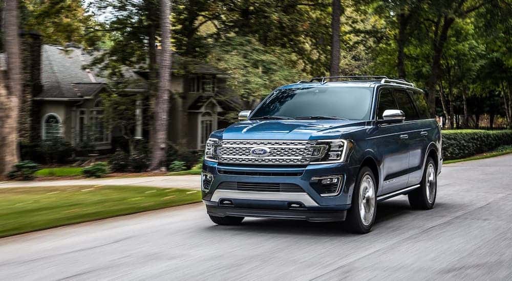 A blue 2020 Ford Expedition is driving on a suburban street.