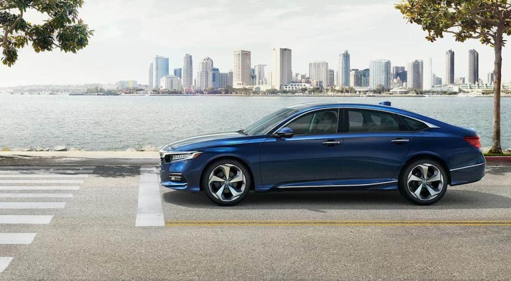 A blue 2020 Honda Accord is stopped at a crosswalk with a city in the distance.