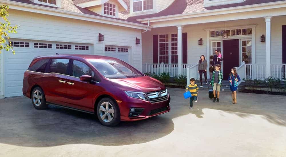 A family is walking toward their red 2020 Honda Odyssey outside a white house.