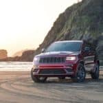 A red 2020 Jeep Grand Cherokee is parked on a beach at sunset.