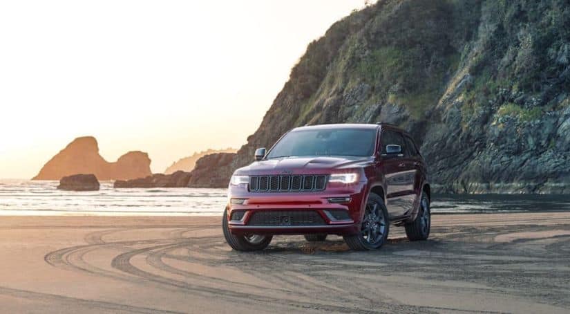 A red 2020 Jeep Grand Cherokee is parked on a beach at sunset.