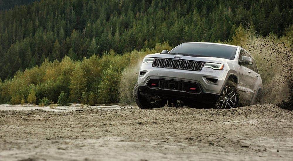 A silver 2020 Jeep Grand Cherokee Trailhawk is driving on a dirt trail in the woods after winning the 2020 Jeep Grand Cherokee vs 2020 Toyota 4Runner comparison.