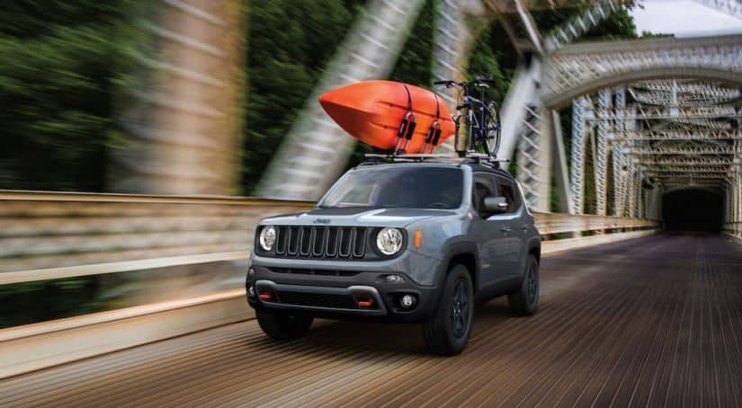A grey 2020 Jeep Renegade is driving on a bridge with a kayak on the roof.
