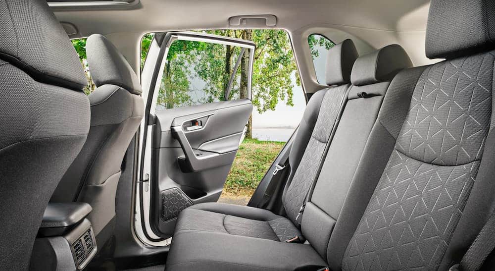 The backseat with grey interior in a 2020 Toyota RAV4 Hybrid XLE is shown with the rear door open.