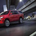 A red 2021 Chevy Tahoe RST is driving under a city bridge at night.