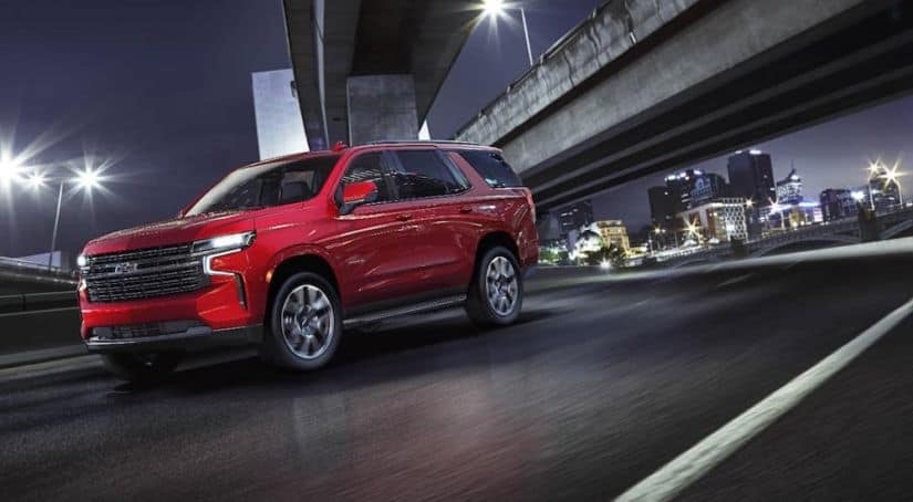 A red 2021 Chevy Tahoe RST is driving under a city bridge at night.