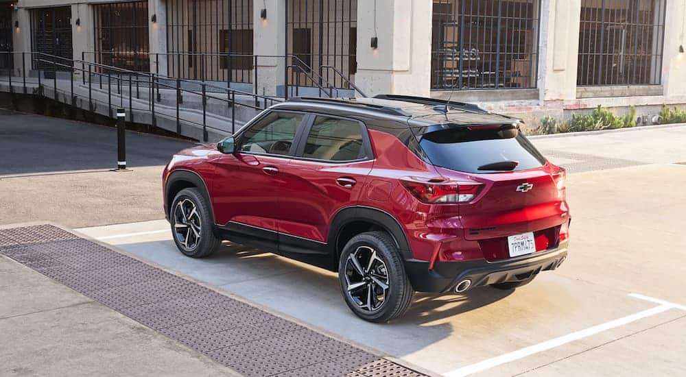 A red 2021 Chevy Trailblazer is parked in front of a white industrial building with large windows during a comparison of the 2021 Chevy Trailblazer vs 2020 Chevy Trax.