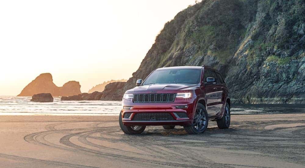 A dark red 2020 Jeep Grand Cherokee from a local Jeep Dealership is parked at a beach.