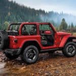 A red 2020 Jeep Wrangler Rubicon is crossing a river in the woods.