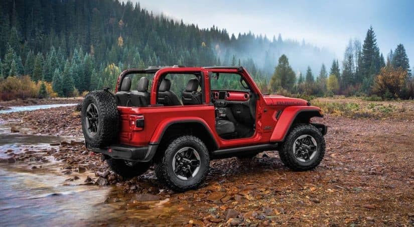 A red 2020 Jeep Wrangler Rubicon is crossing a river in the woods.