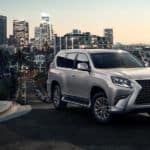 A silver 2020 Lexus GX is parked on a street with a city in the distance.