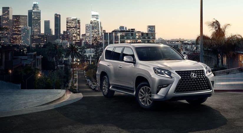 A silver 2020 Lexus GX is parked on a street with a city in the distance.