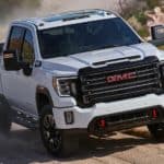 A popular truck for sale, a white 2020 GMC Sierra HD AT4, is shown from the front driving on a dirt road.