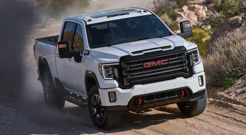 A popular truck for sale, a white 2020 GMC Sierra HD AT4, is shown from the front driving on a dirt road.