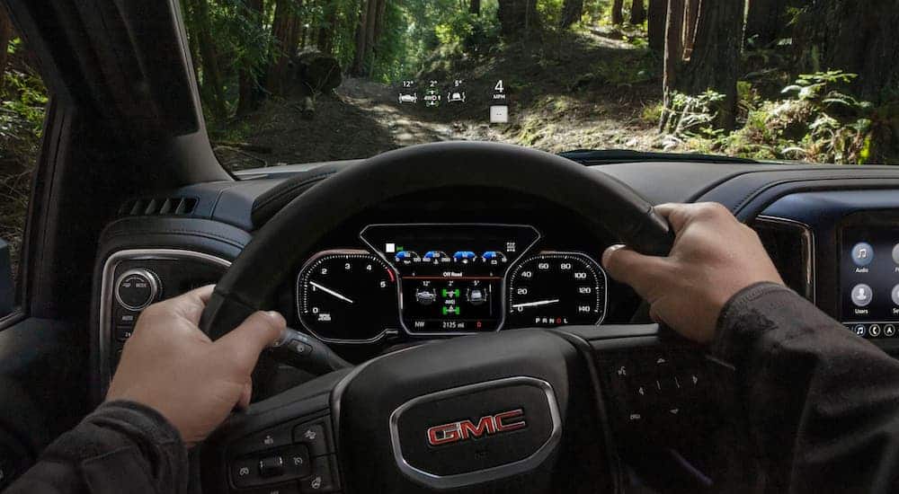 A driver's point of view is showing the head up display in a 2020 GMC SierraHD AT4 which is driving through the woods.