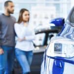 A couple is out of focus behind a blue vehicle at a used car dealer near me.