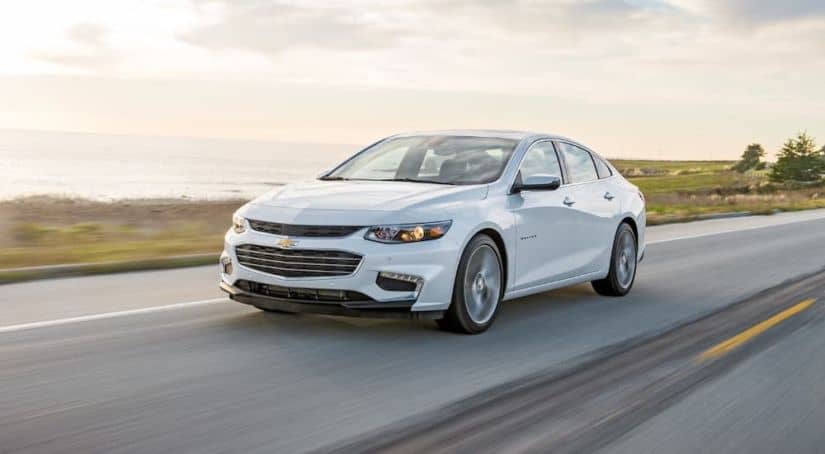 One of the popular used cars to find online, a white 2018 Chevy Malibu, is driving on a coastal highway.