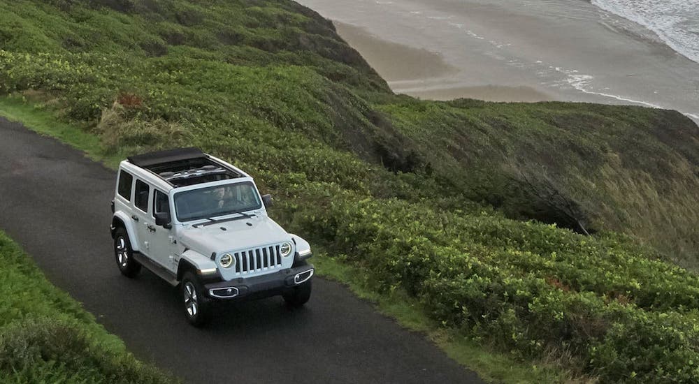 A white 2019 Jeep Wrangler Unlimited is driving on a mountainous road with its roof open and shown from a high angle.