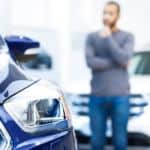 A man is out of focus while looking at a blue used car near me.