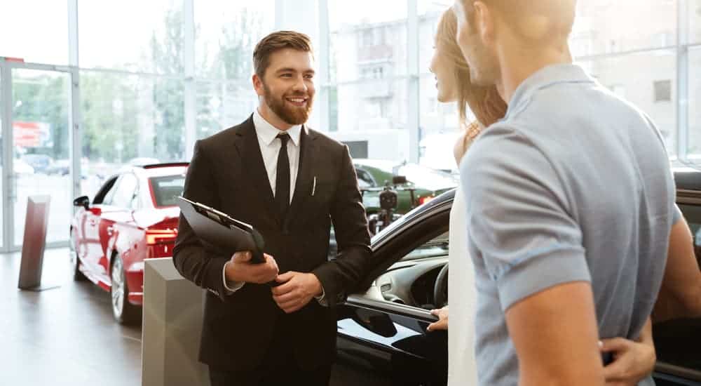 A couple is talking to a car salesman in a suit.